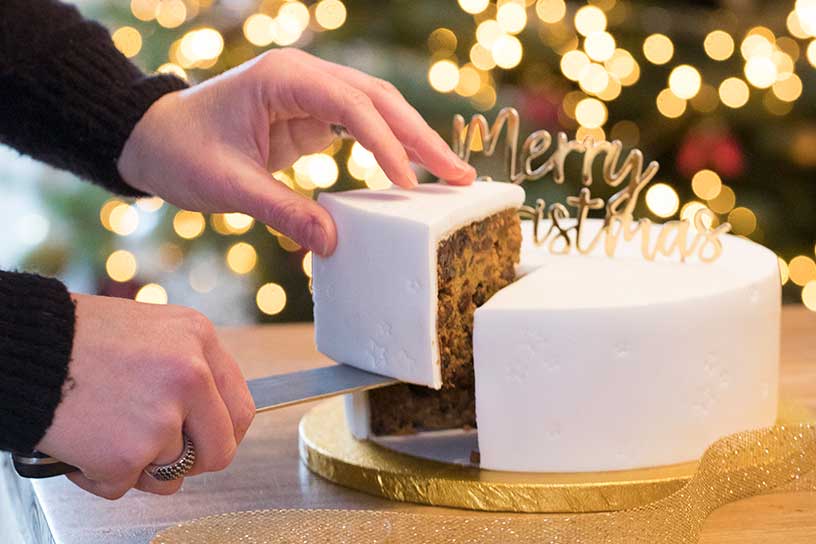 Twee handen die met een mes een kersttaart aansnijden